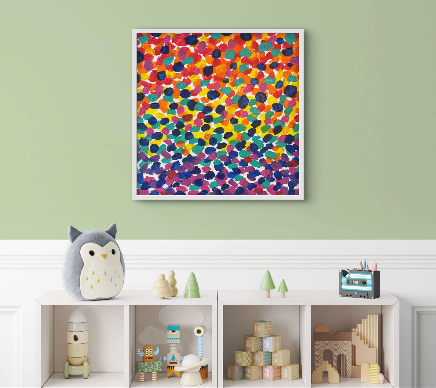 Colorful abstract art piece on a green wall above a shelf with toys.