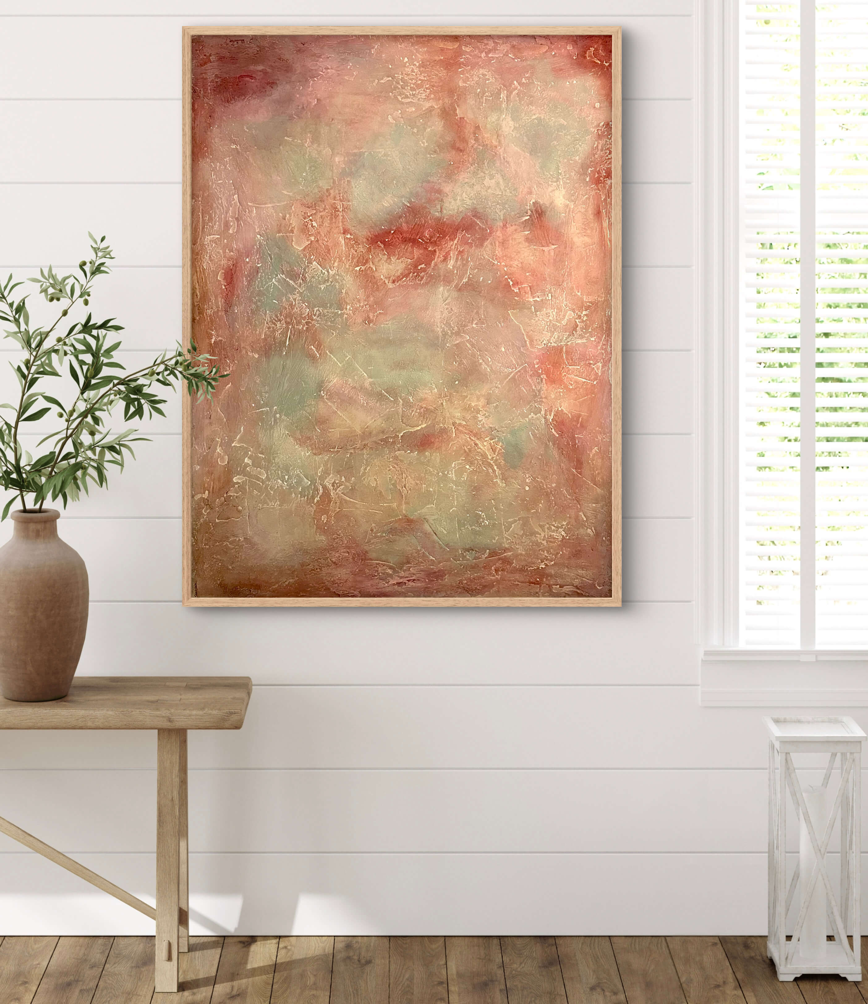 Abstract painting on a white wall with a wooden table and plant in the foreground.